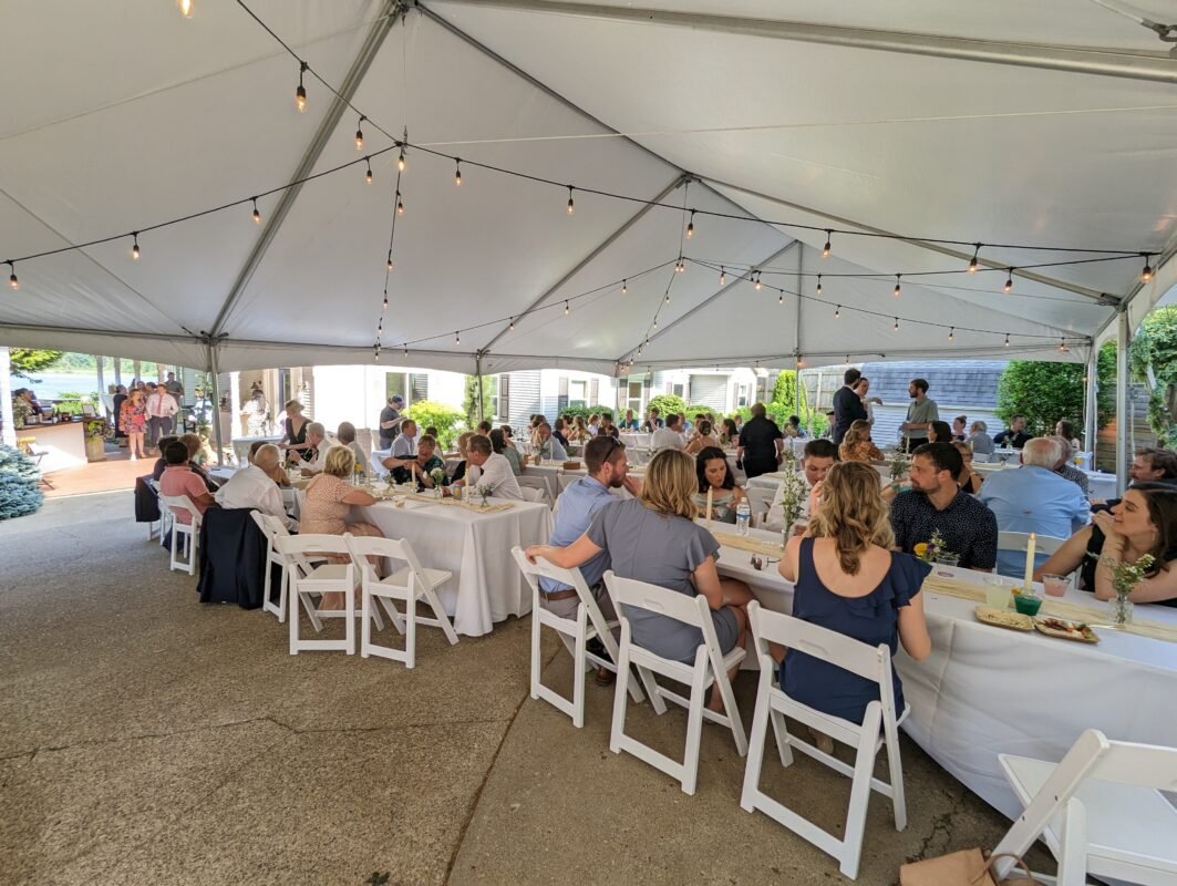 An image of a white tent, string lights overhead, and wedding attendees sitting at tables underneath.